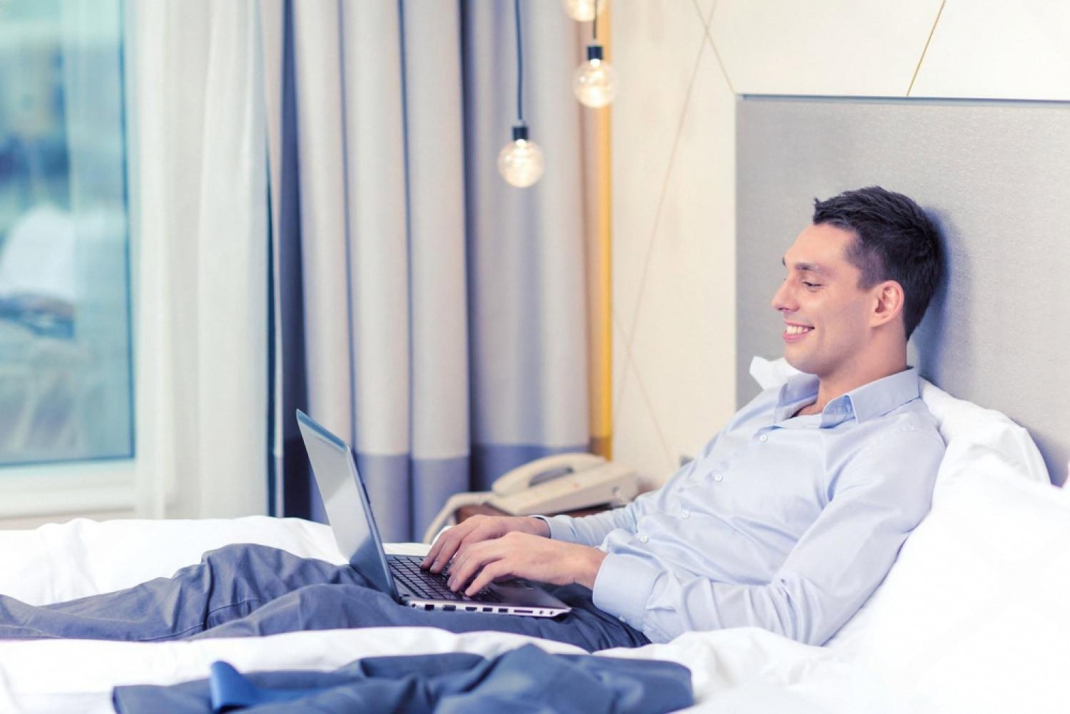 Business traveller using a laptop on a hotel bed in Dubai to complete online check-in